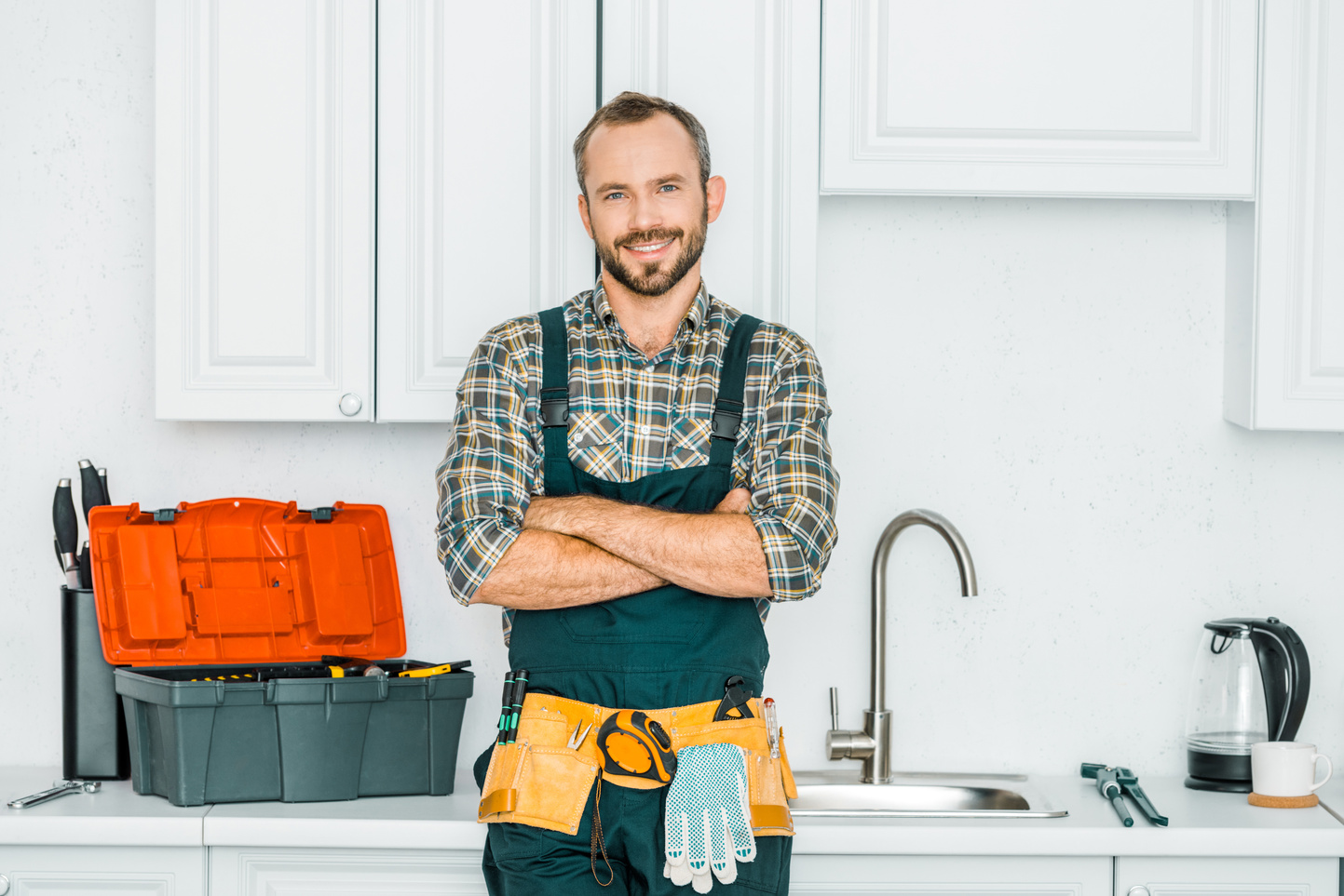 smiling handsome plumber standing with crossed arms and looking at camera in kitchen